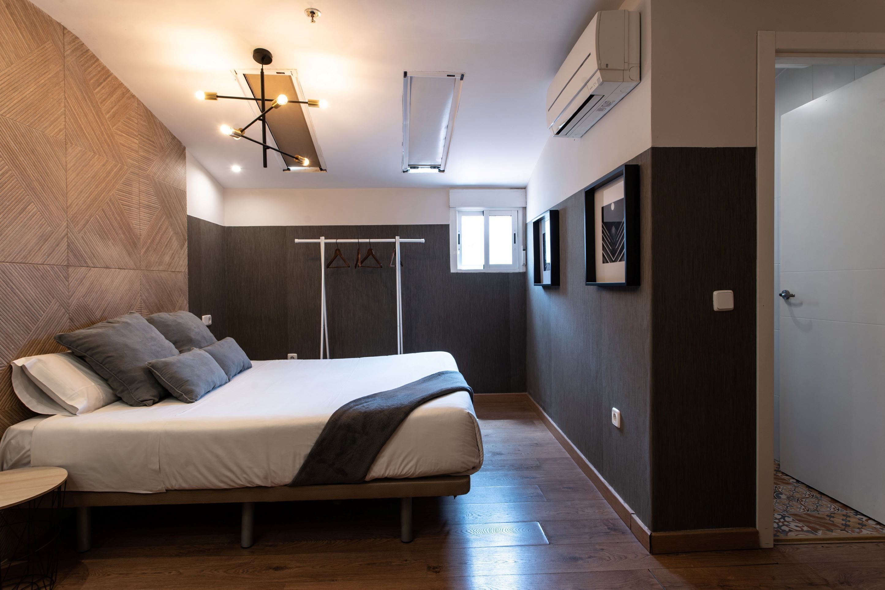 Ein Schlafzimmer mit Bett, Kleiderstange, Fenster und Tür.