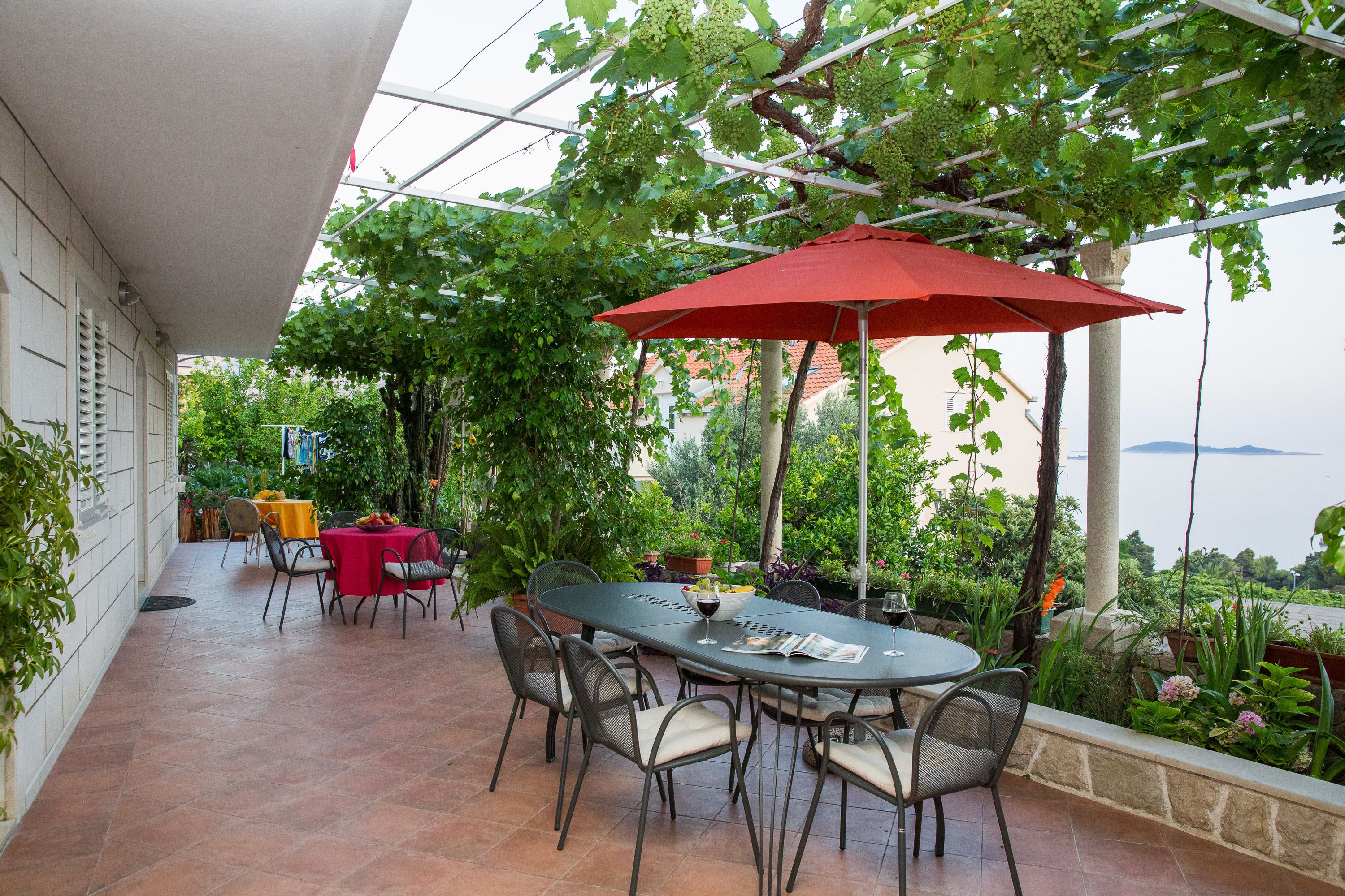 An outdoor patio with a table and chairs, a red umbrella, and a view of the sea.