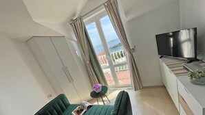 Une petite pièce moderne, dotée d’un canapé vert, d’un téléviseur et offrant une vue sur un balcon avec une balustrade.