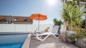 Une piscine avec deux chaises longues blanches et un parasol orange.