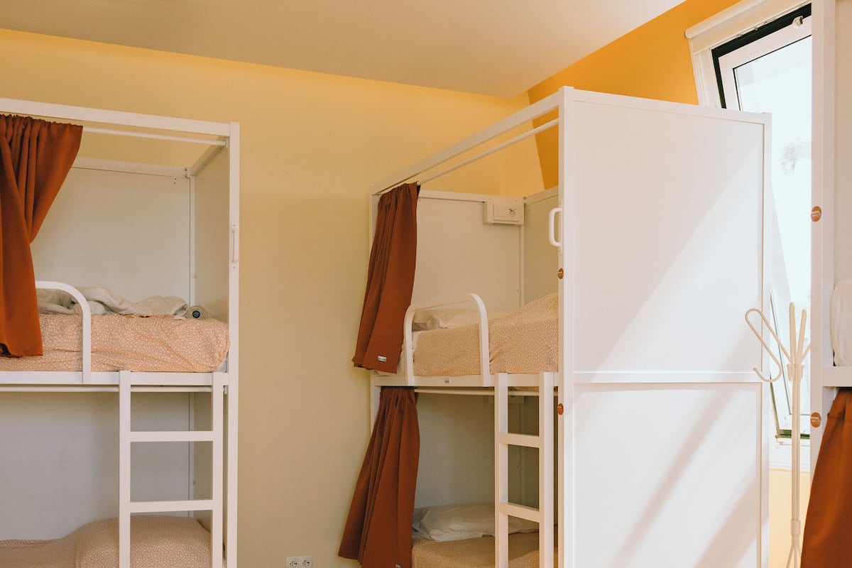 Un dormitorio con literas, suelo de madera y un armario blanco.