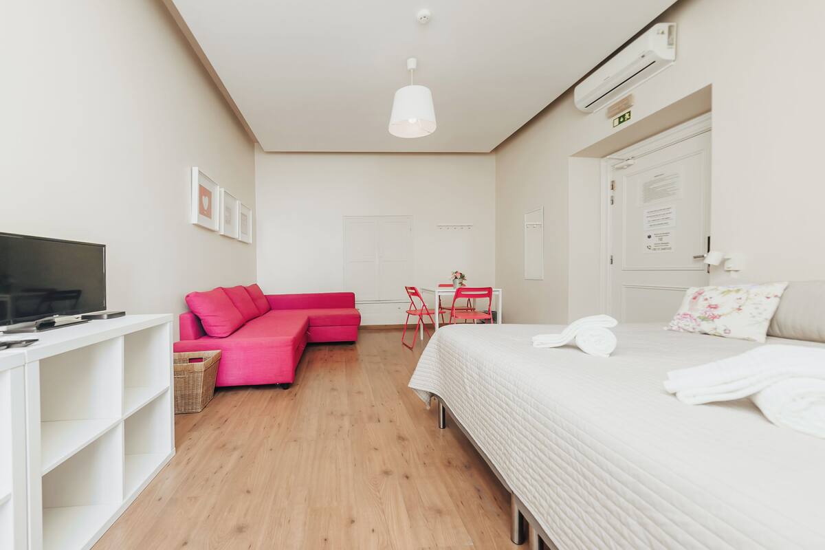 Una habitación de hotel moderna con una cama, un televisor, un sofá rojo, una mesita y una silla.