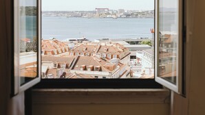 Vista a través de una ventana abierta de un paisaje urbano costero con edificios y una masa de agua.