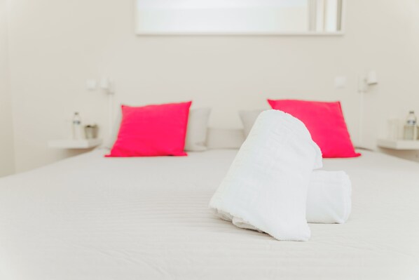 Habitación de hotel con una cama bien hecha, dos almohadas rojas brillantes y una toalla blanca sobre la cama.