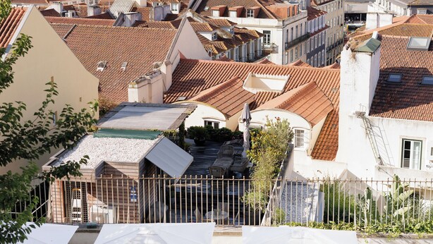 Un patio con sombrillas blancas y sillas, rodeado de edificios con techos de tejas rojas.