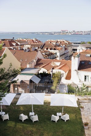A courtyard with white umbrellas and chairs, surrounded by buildings with red-tiled roofs. - Lisb'on Hostel (Lisbon)