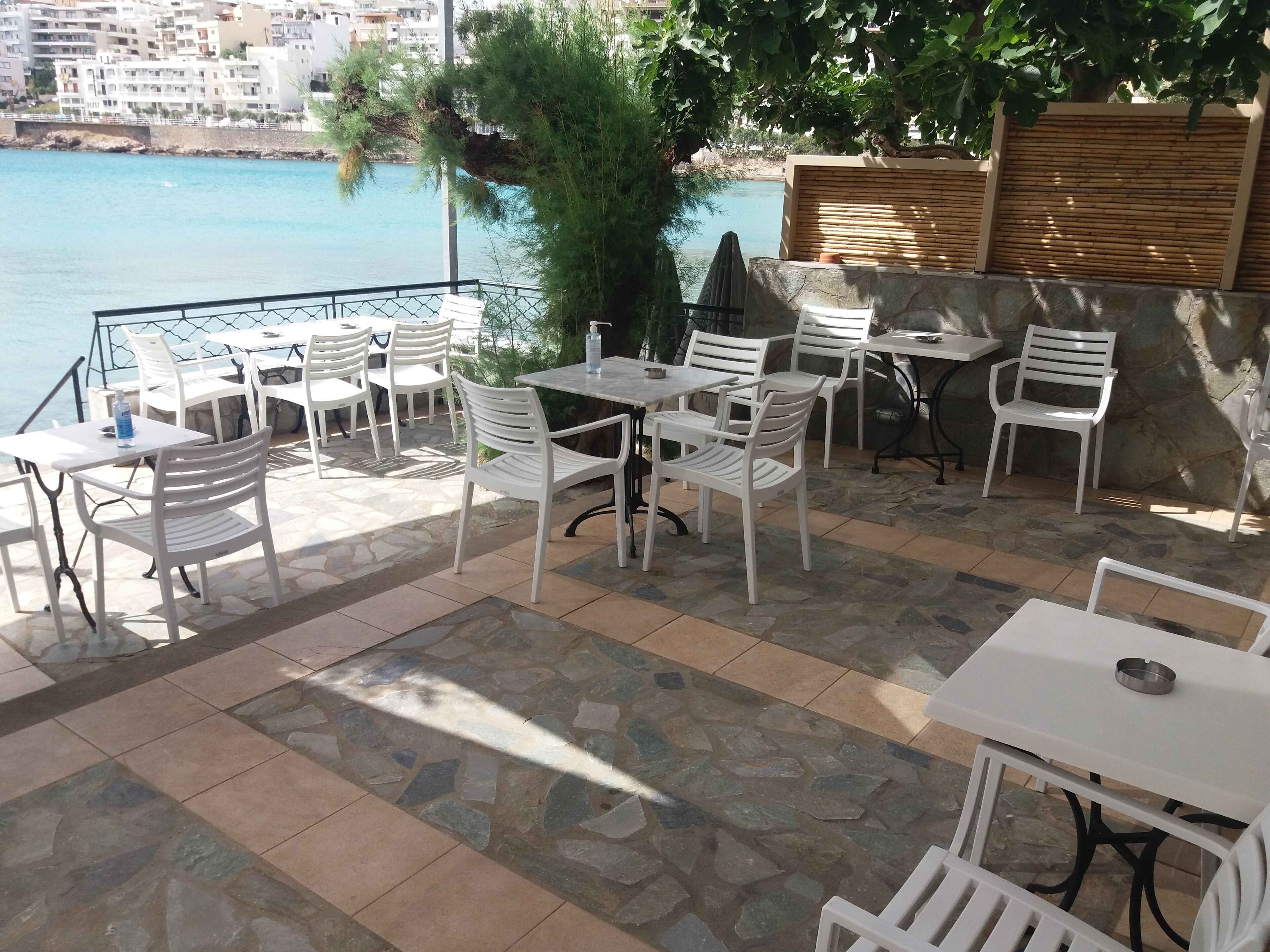An outdoor seating area with stone flooring and white furniture, overlooking a body of water and a coastal cityscape.