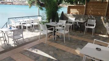 An outdoor seating area with stone flooring and white furniture, overlooking a body of water and a coastal cityscape.