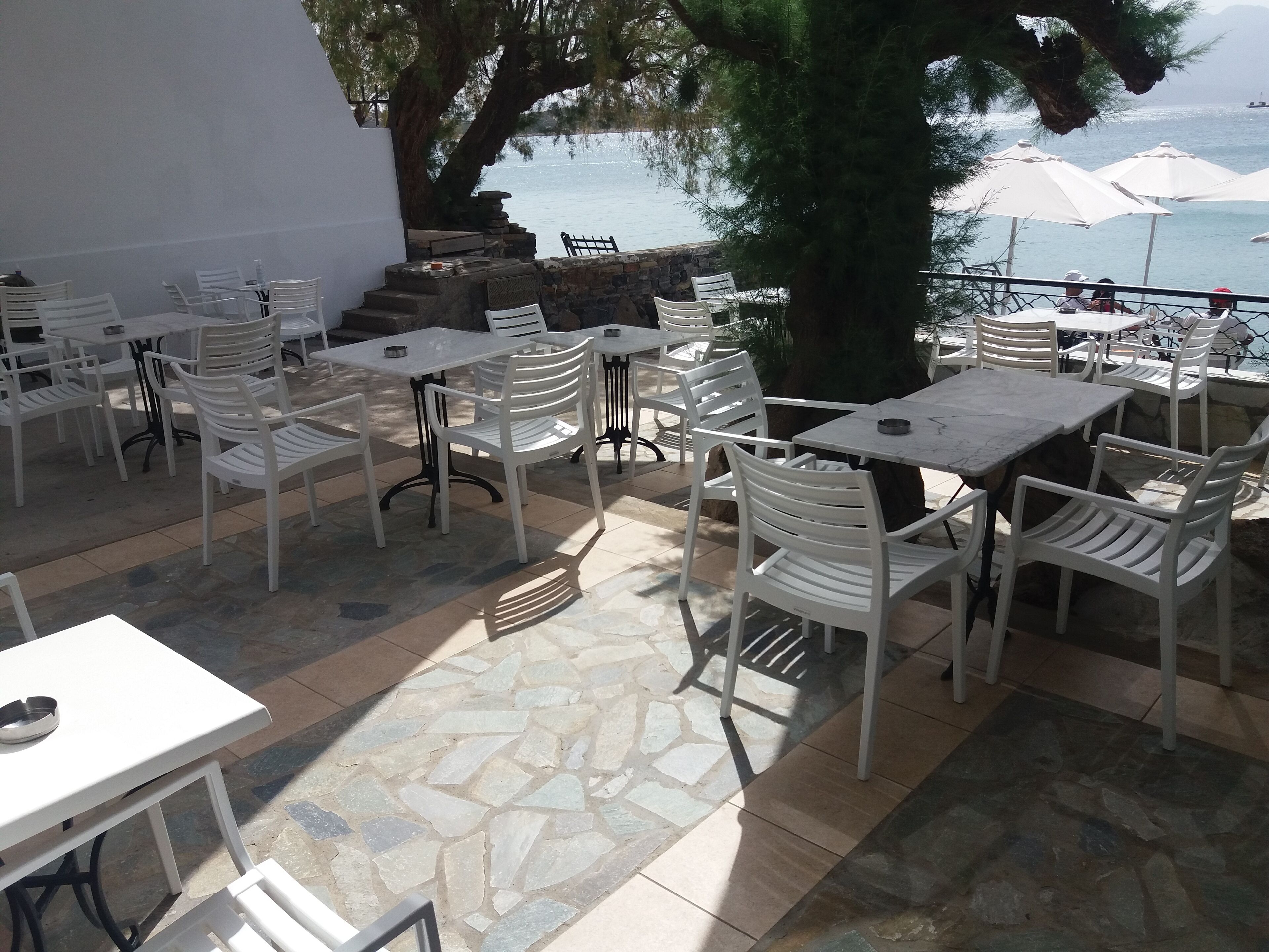 An outdoor patio with stone flooring, white tables and chairs, and umbrellas.
