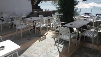 An outdoor patio with stone flooring, white tables and chairs, and umbrellas.