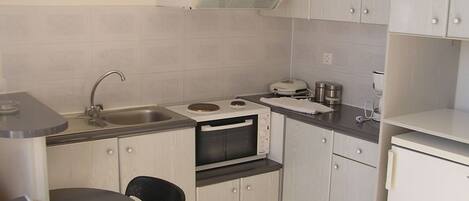 A compact kitchen with a sink, stove, microwave, and a small refrigerator.