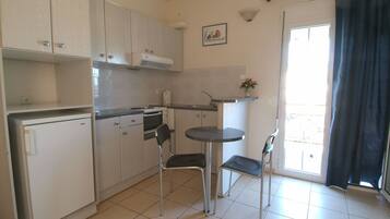 A compact kitchen with white cabinets, a small refrigerator, a sink, and a dining area with two chairs and a small table.