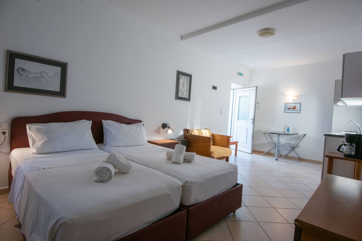 Habitación de hotel con dos camas, un escritorio, una silla y una mesita.
