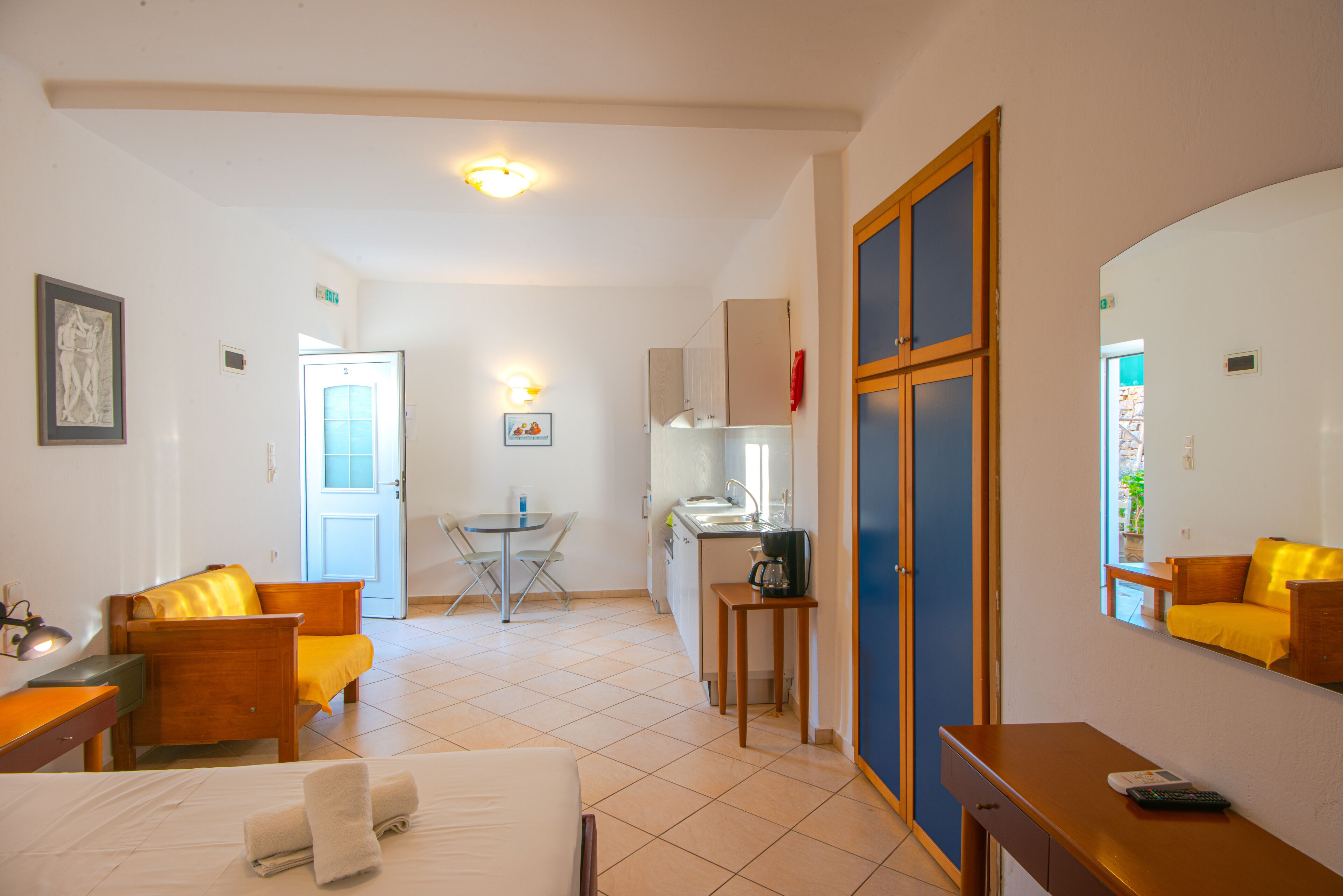 Une chambre d’hôtel comprenant un lit, un bureau, une chaise, une petite table, un coin cuisine et une salle de bain avec un miroir.