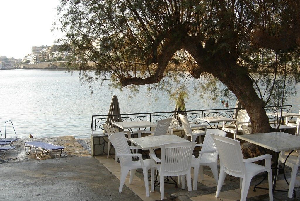A waterfront outdoor seating area with tables and chairs, overlooking a body of water.