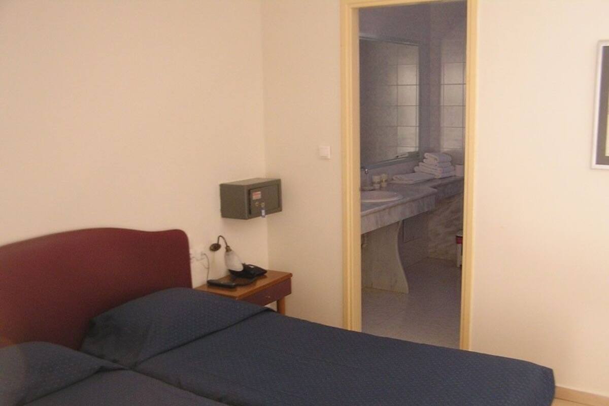 Un dormitorio con cama, mesita de noche, lámpara y espejo.