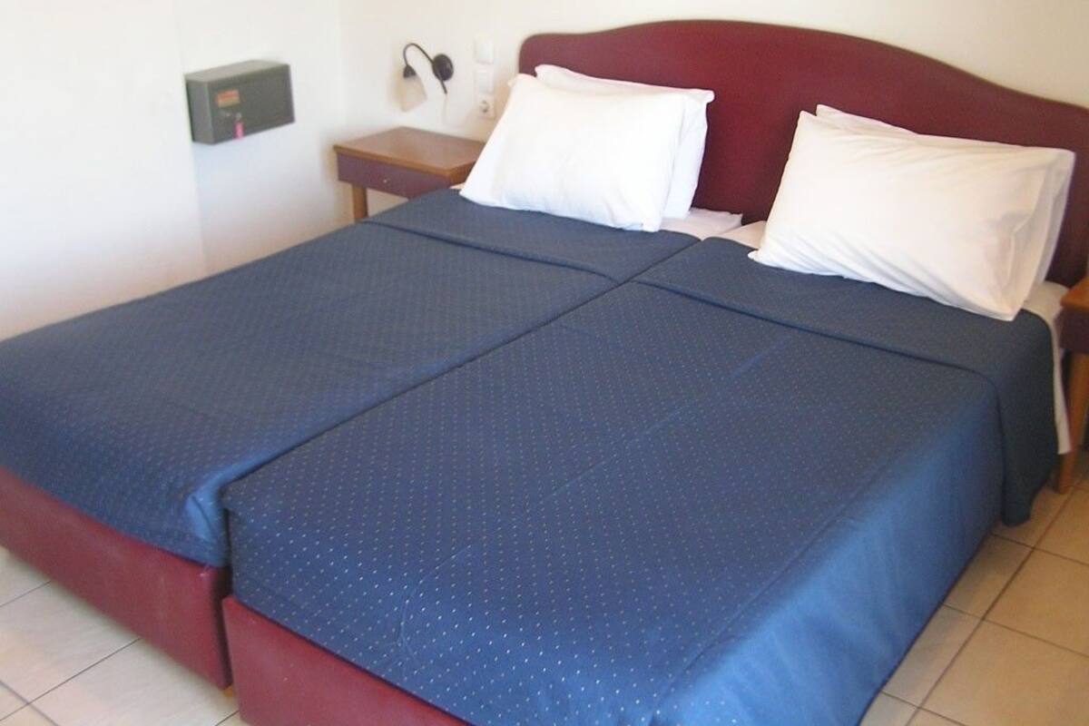 Una cama doble con cabecera roja, dos almohadas blancas y una colcha azul.