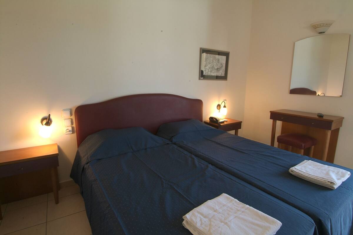 Una habitación con dos camas, un escritorio, una silla, un espejo y lámparas de noche.