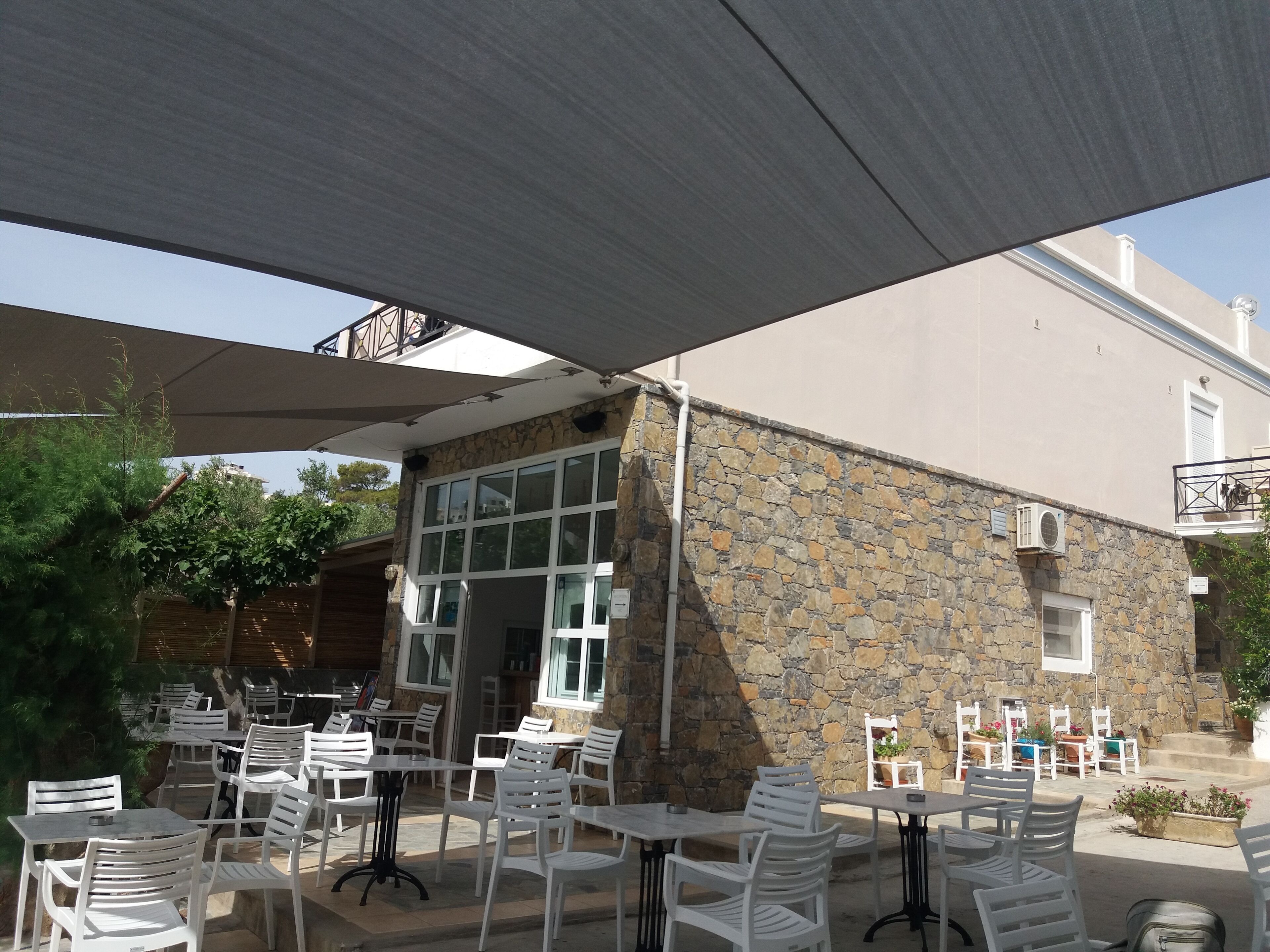 An outdoor patio area with white plastic chairs and tables, stone walls, and a covered section with a canopy.