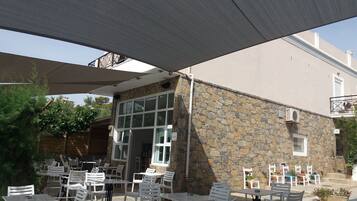 An outdoor patio area with white plastic chairs and tables, stone walls, and a covered section with a canopy.