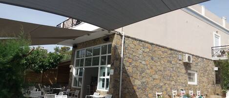 An outdoor patio area with white plastic chairs and tables, stone walls, and a covered section with a canopy.