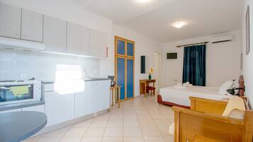 A compact hotel room with a kitchenette, a single bed, a small table, and a bedside table.