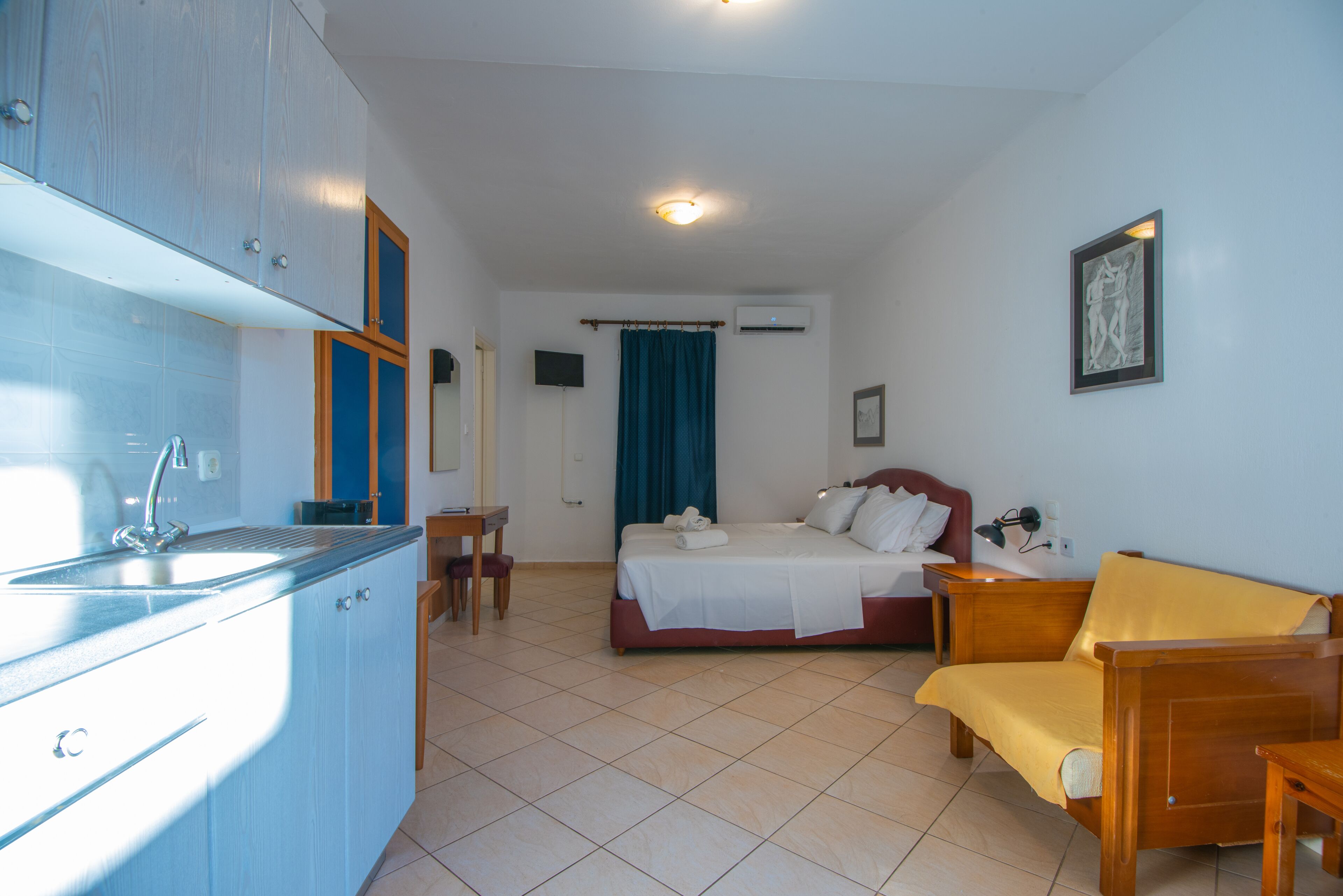 A hotel room with a bed, a sofa, a desk, a chair, a sink, and a television.