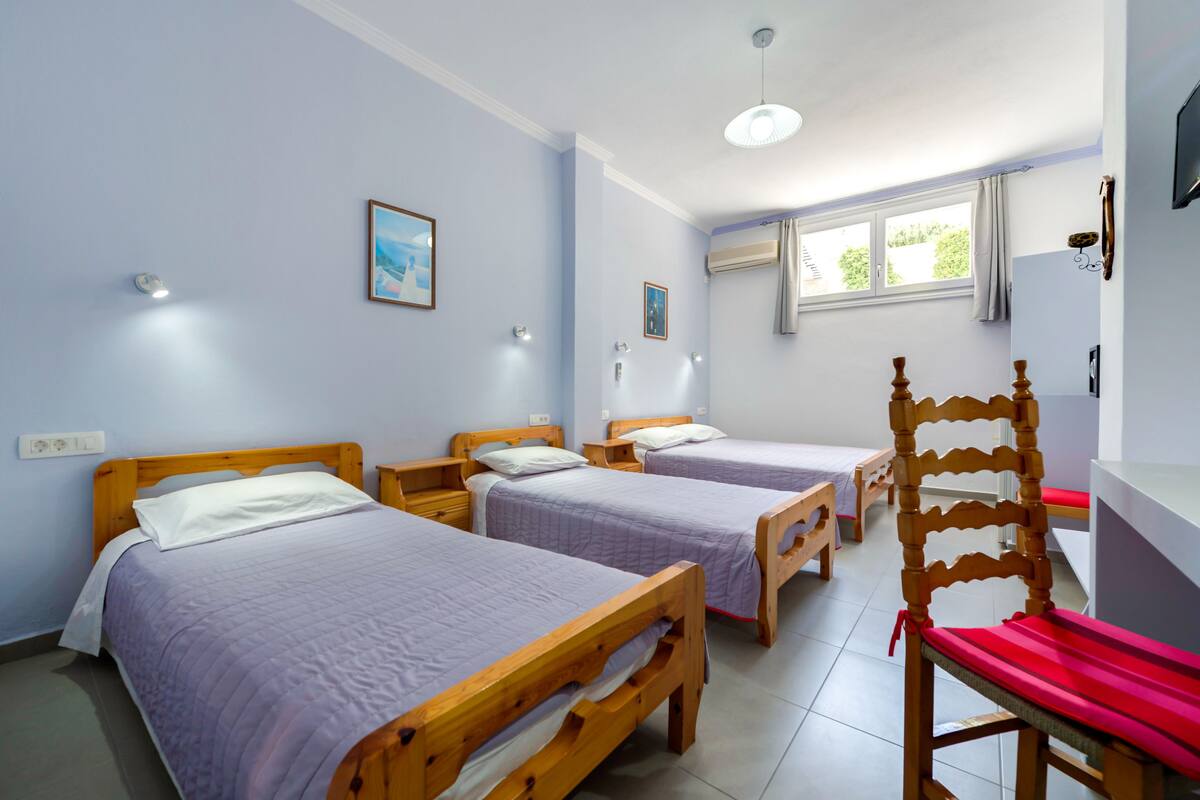 A room with two wooden beds, a wooden chair, a white desk, and a window with curtains.
