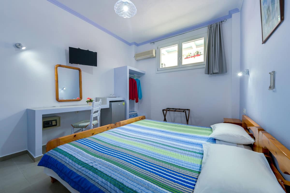 A bedroom with a bed, a desk, a TV, and a window with curtains.