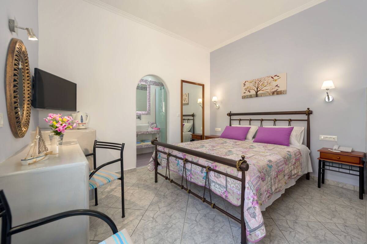 A bedroom with a bed, bedside table, lamp, and a desk with a chair.