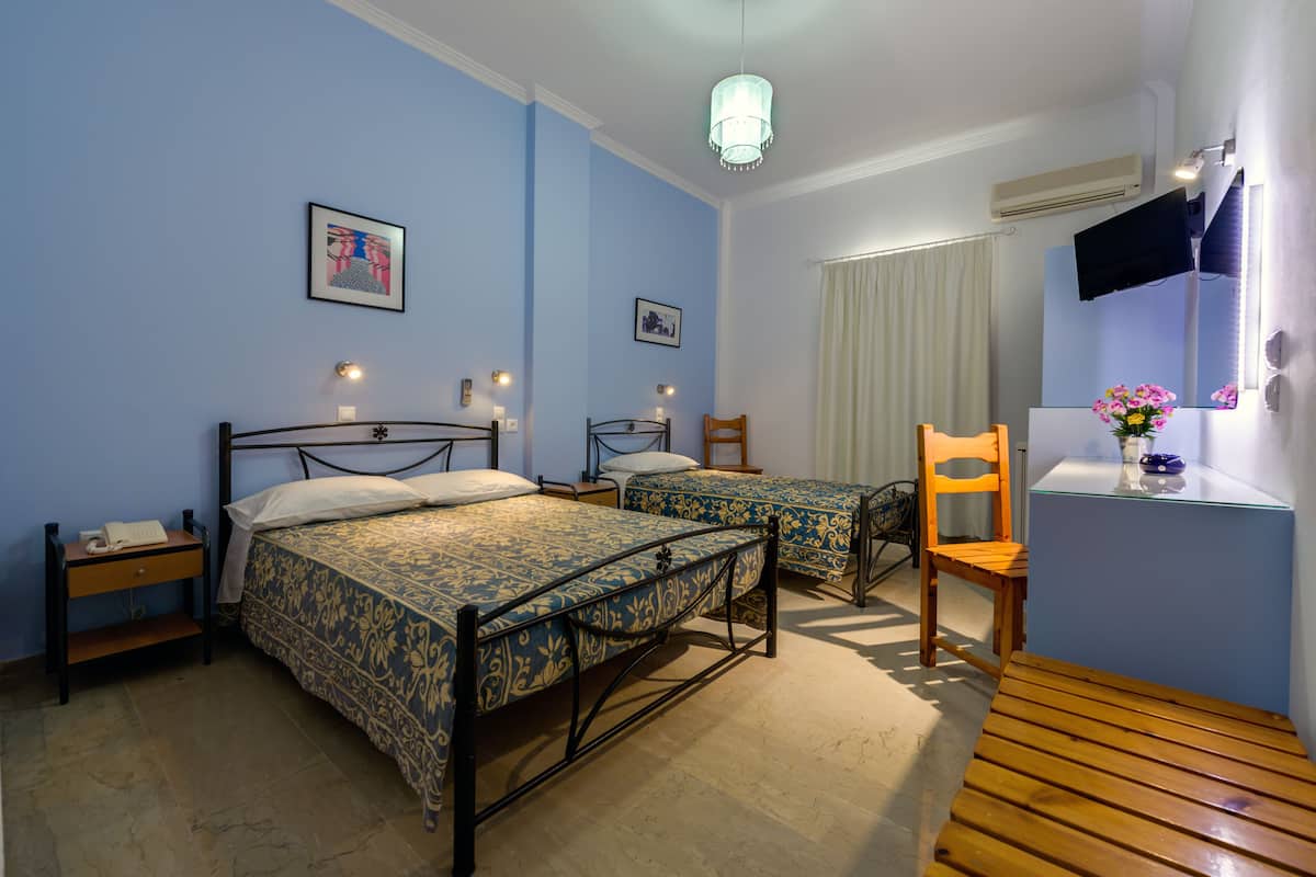 A hotel room with two beds, a wooden chair, a small table, and a TV mounted on the wall.