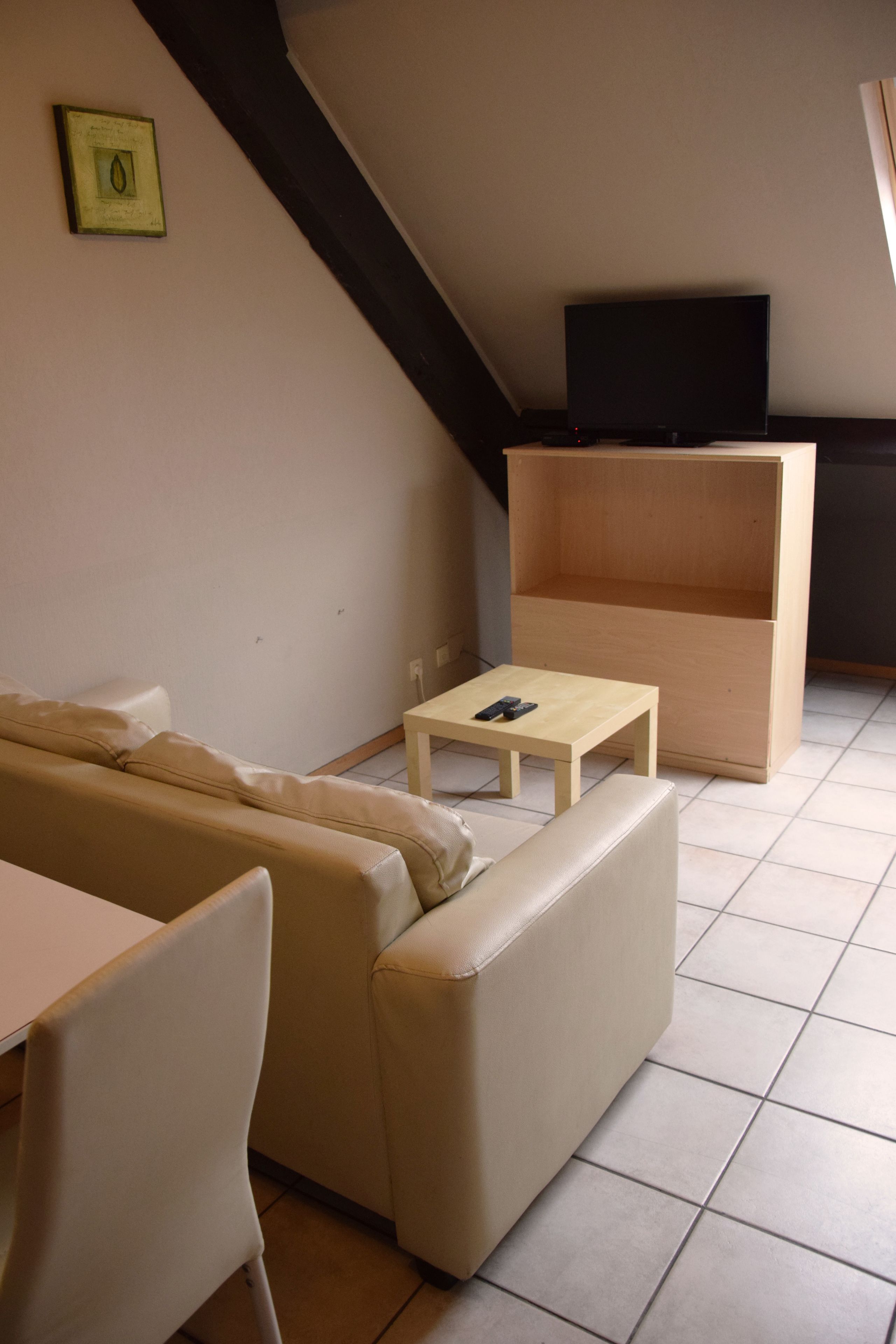 A living room with a sofa, a small table, a television on a stand, and a wooden shelf.
