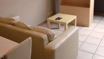 A living room with a sofa, a small table, a television on a stand, and a wooden shelf.