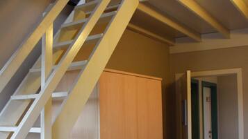 A staircase with a wooden finish and white railings, leading to a room with a wooden wardrobe and a tiled floor.