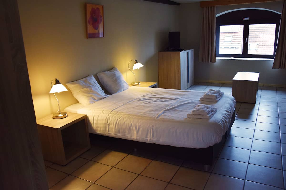 A neatly made bed with two bedside tables, each with a lamp, a wooden cabinet, and a window with curtains.