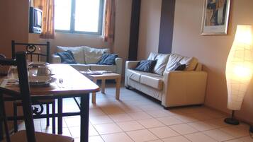 A living room with a dining table, two sofas, a TV, and a lamp.