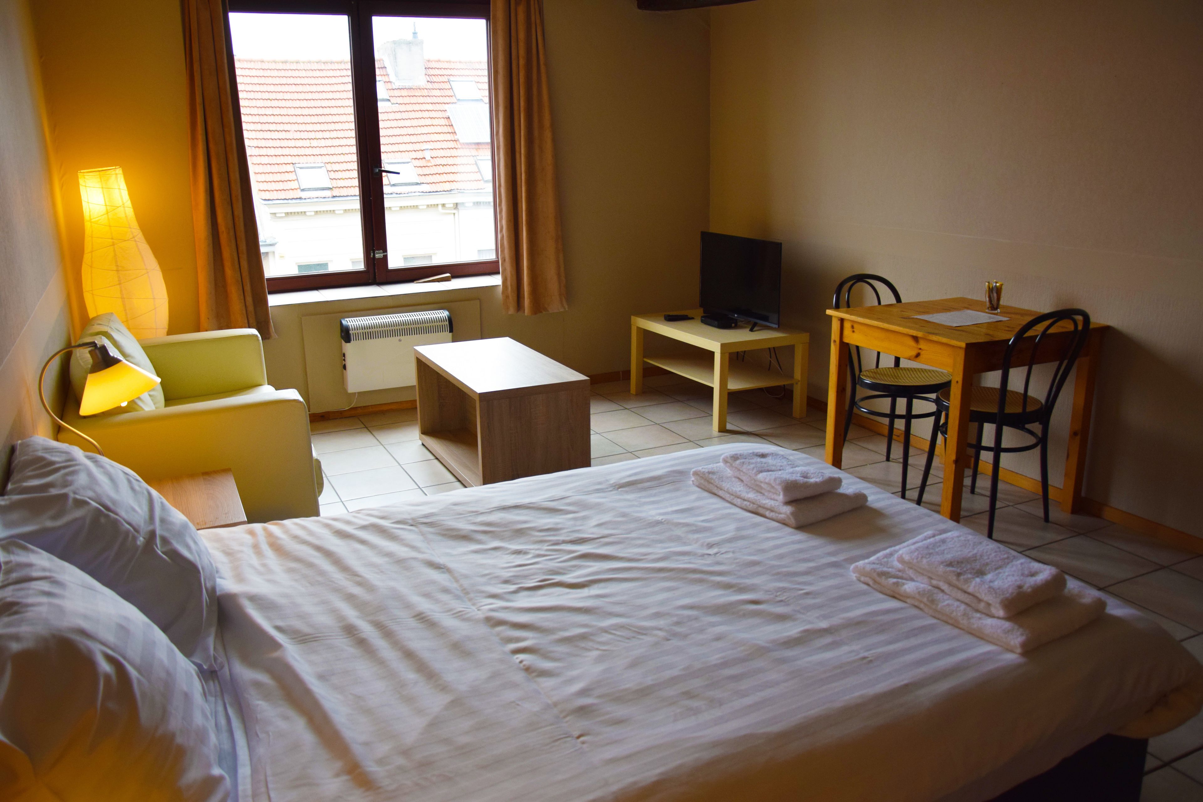 Ein Hotelzimmer mit einem Bett, einem Schreibtisch, einem Sessel, einem Fernseher und einem Vorhangfenster.