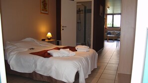 Habitación de hotel con una cama grande, una mesita de noche con lámpara, zona de ducha y vistas al exterior.