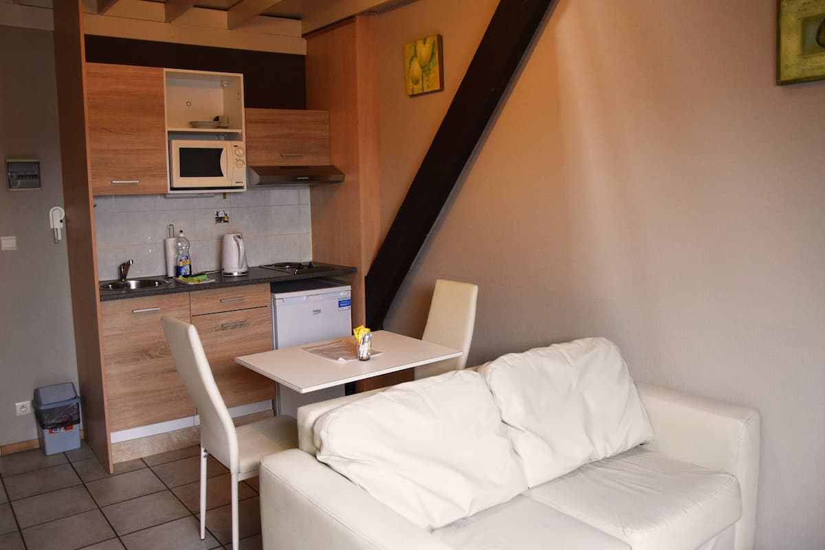 A compact kitchenette with a microwave, sink, and small refrigerator. There is a white sofa and a dining table with chairs in the living area.