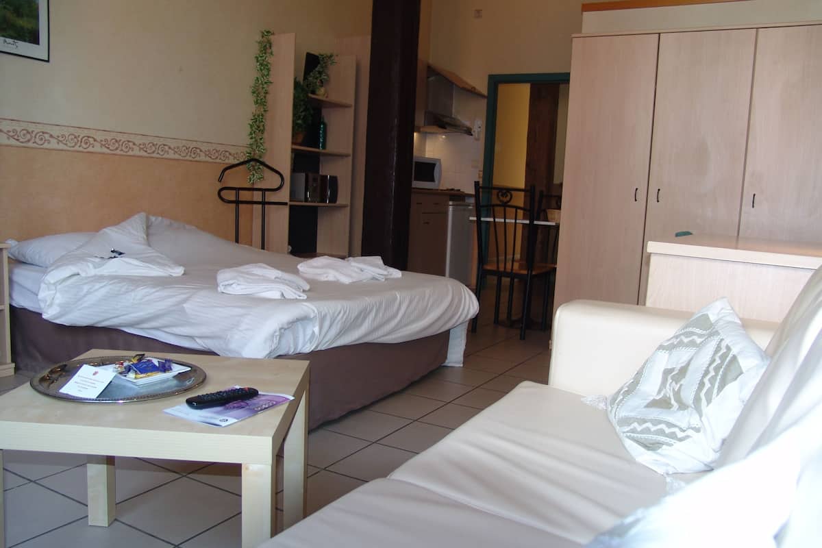 A hotel room with a bed, a small table with a tray, a chair, a sofa, and a wardrobe.