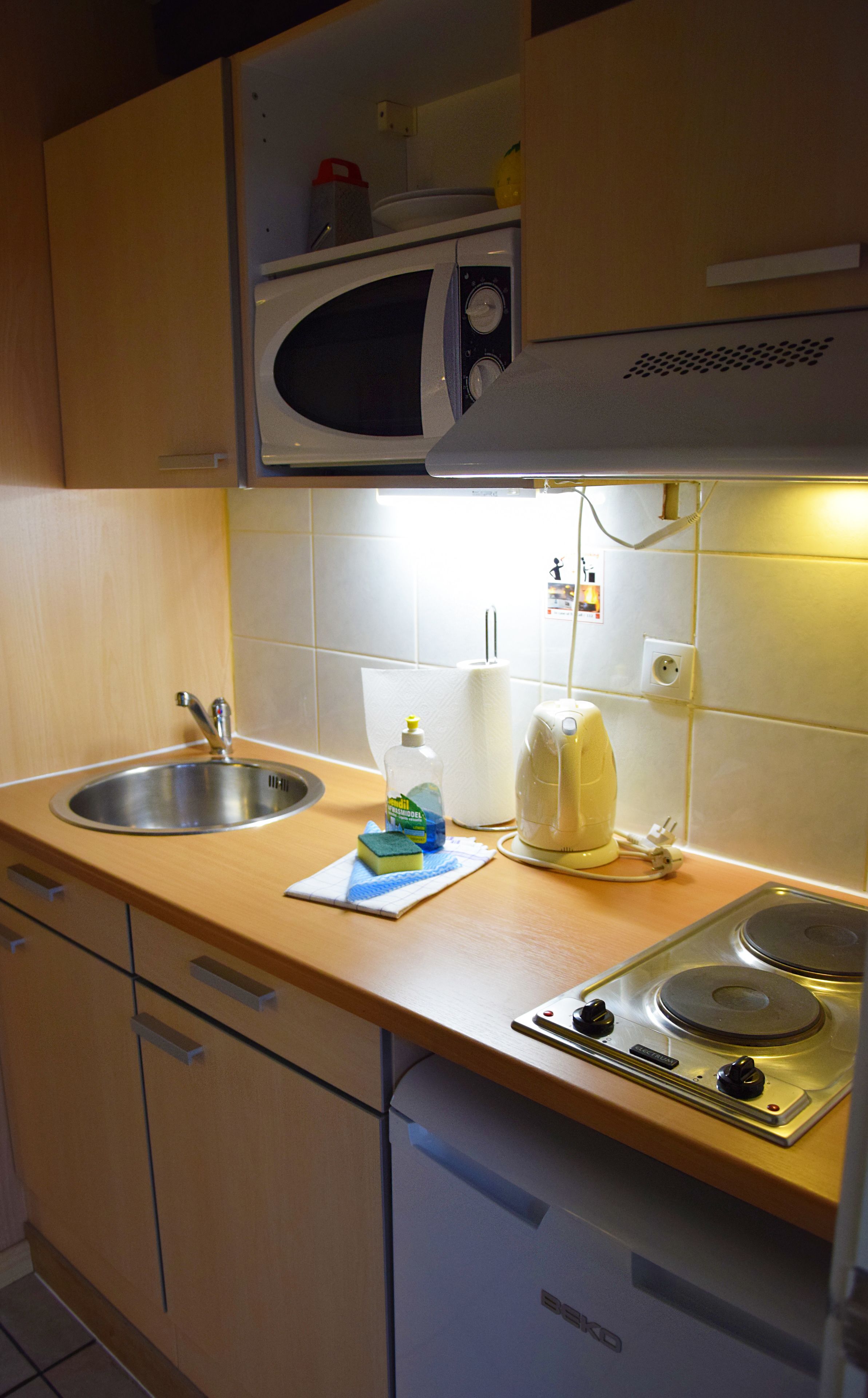 Uma cozinha compacta com micro-ondas, pia e fogão pequeno.