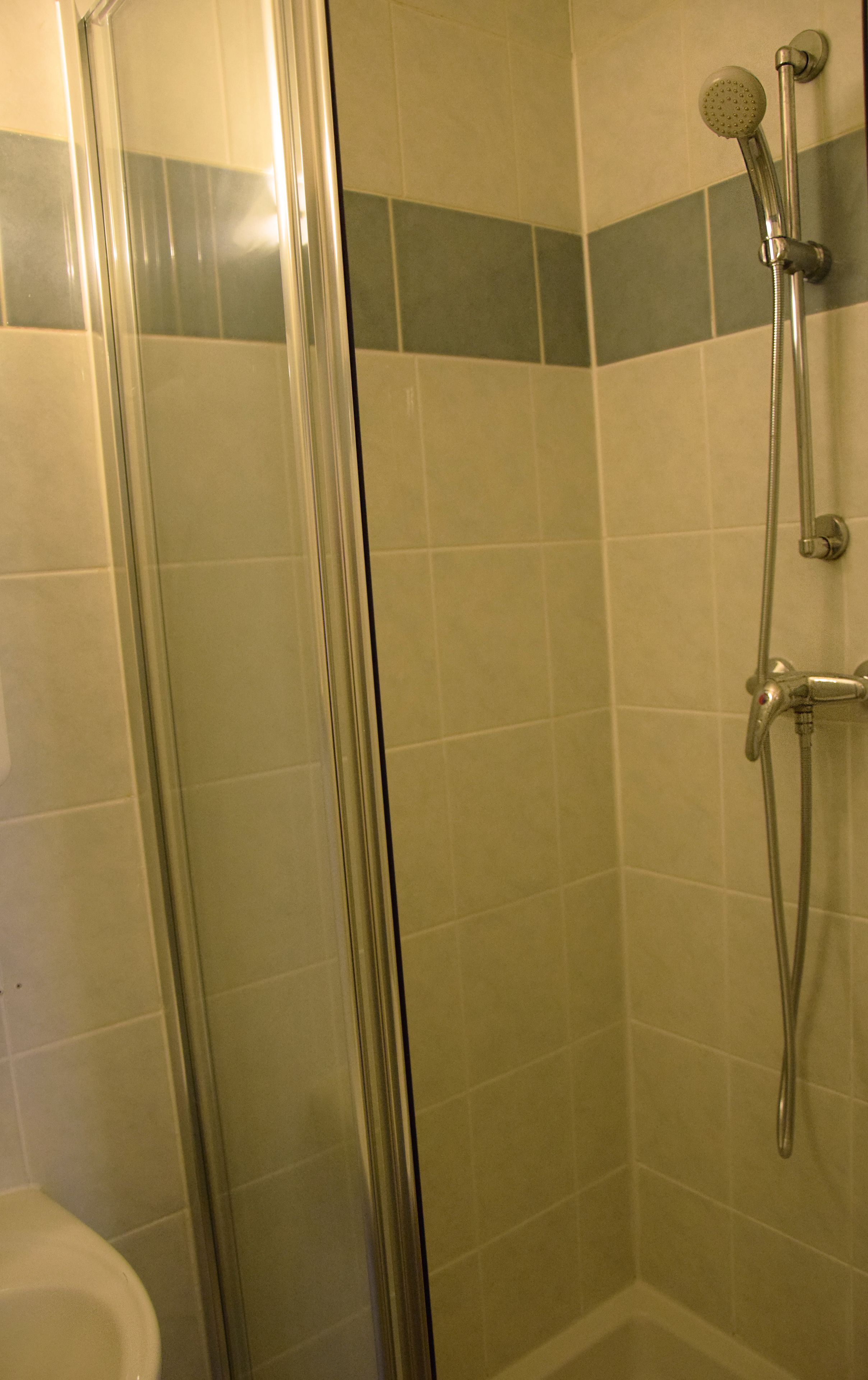 Un espace douche doté d’une porte en verre, d’un pommeau de douche à main et d’un robinet mural.