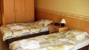 A hotel room with two single beds, a wooden wardrobe, a nightstand with a lamp, and a decorative wall border.