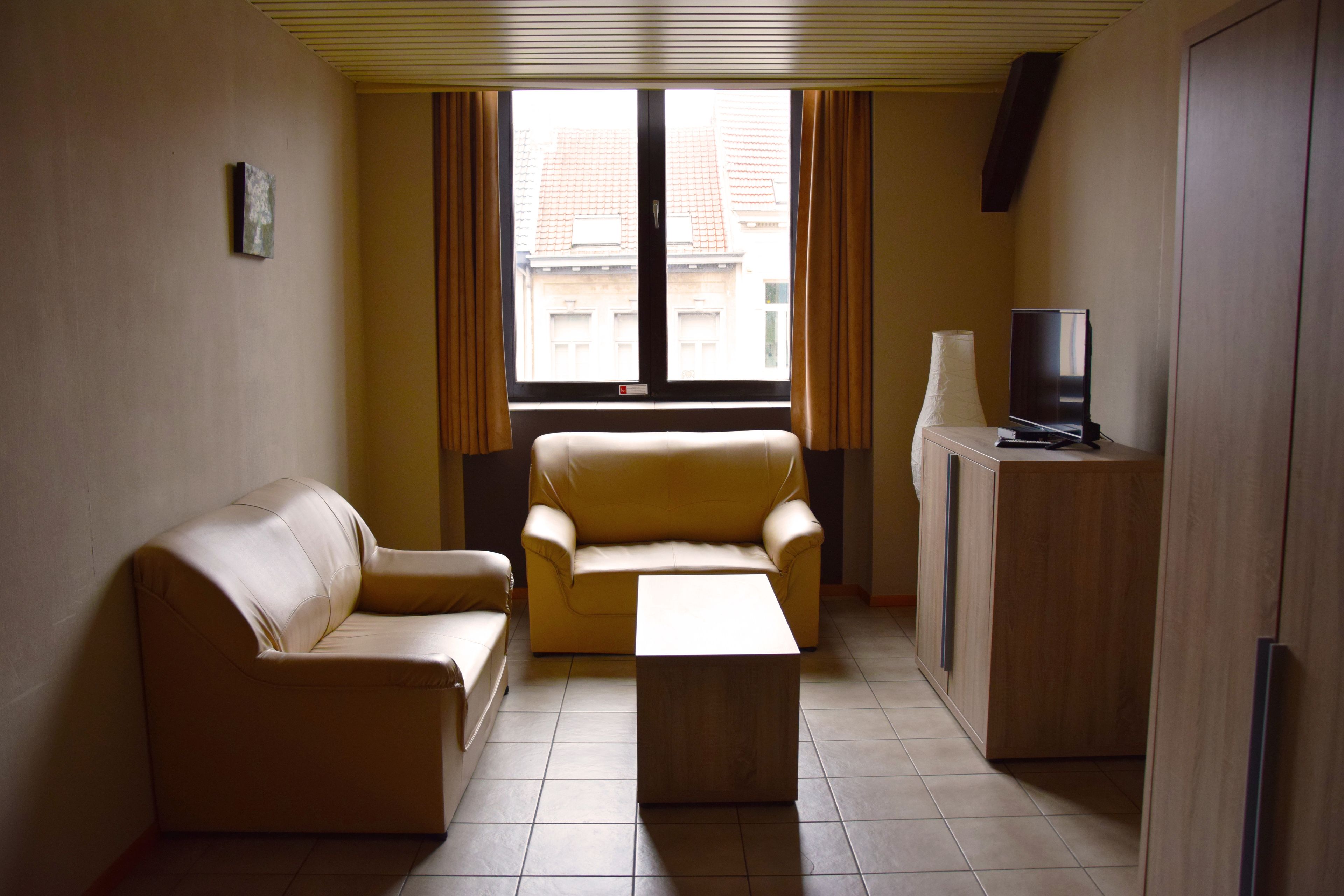 Un salon avec un canapé, une table basse, un téléviseur et une fenêtre avec des rideaux.