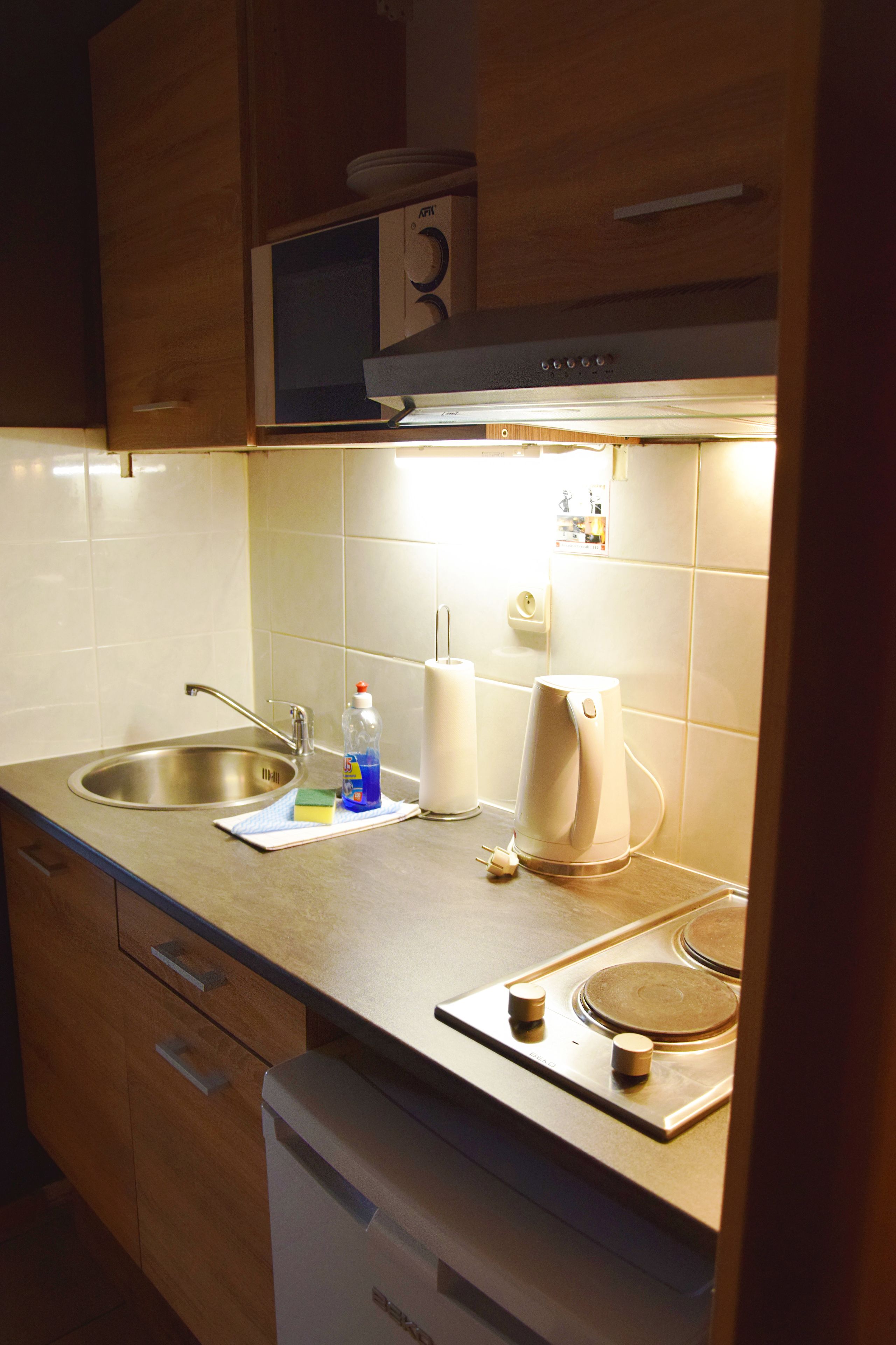 A kitchen with a stainless steel sink, a microwave, a kettle, and a dish soap bottle on the counter.