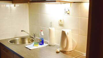 A kitchen with a stainless steel sink, a microwave, a kettle, and a dish soap bottle on the counter.