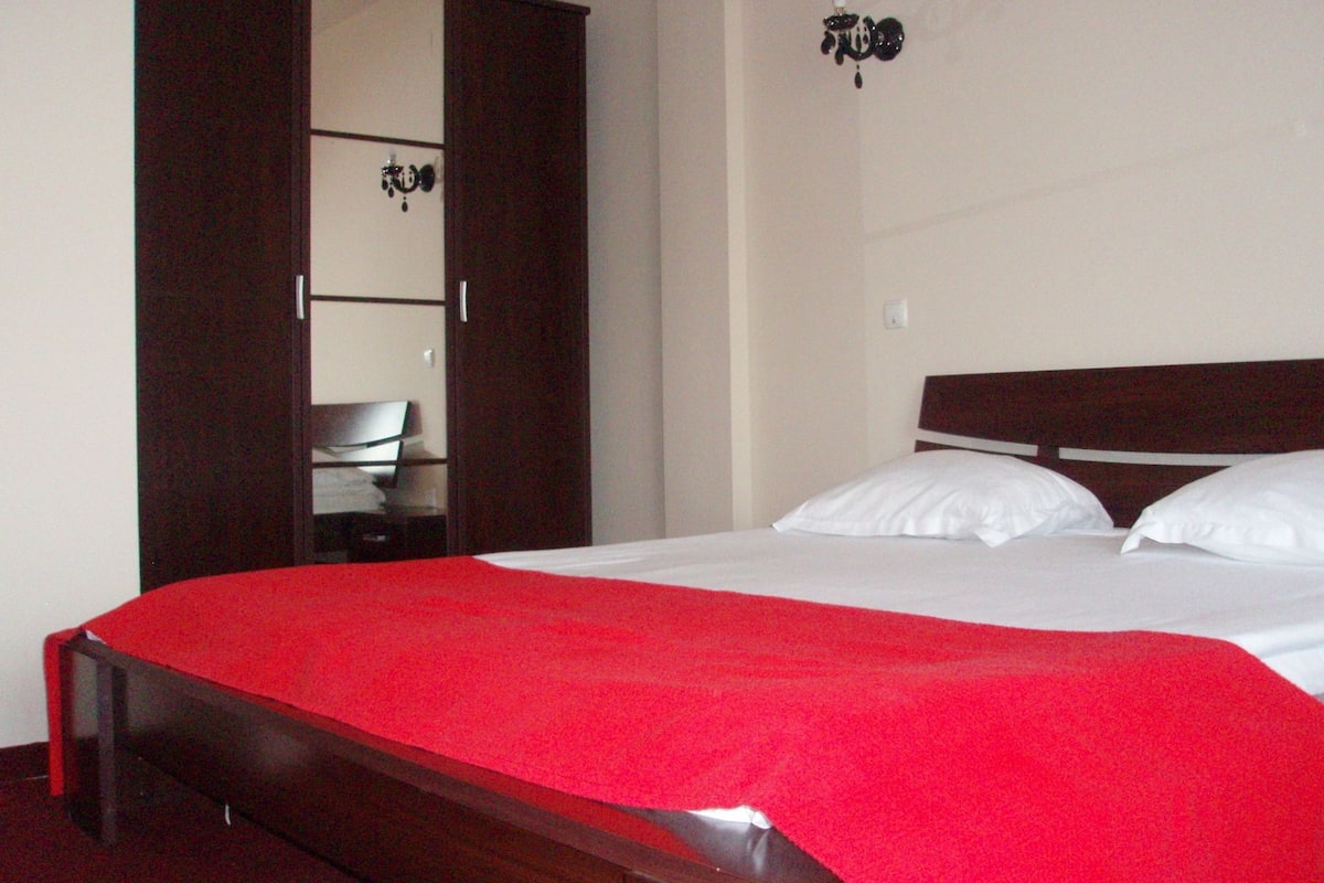 Un dormitorio con cama de madera, almohadas blancas y manta roja.
