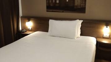 Habitación de hotel con una cama grande, dos mesitas de noche con lámparas, un cuadro en la pared y un par de pantuflas sobre la cama.