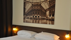 A hotel room with a large bed, two bedside lamps, a nightstand with a phone, and a wall-mounted picture of a historic building. - Nuovo Hotel Italia (Abbiategrasso)