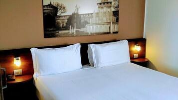 Habitación de hotel con una cama grande, dos mesitas de noche con lámparas, un cuadro en la pared de un edificio histórico y suelo de madera.